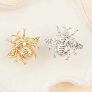 Peut inclure: Deux broches en forme d'abeille, l'une dor&eacute;e et l'autre argent&eacute;e, avec des ailes d&eacute;taill&eacute;es et un corps textur&eacute;.