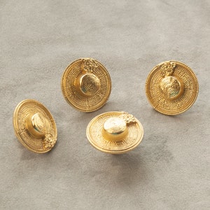 May include: Four gold-coloured metal buttons shaped like miniature straw hats with a floral design.
