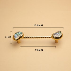 May include: Gold cabinet hardware with a twisted bar and two iridescent shell-shaped knobs. The hardware measures 134 mm long and 96 mm wide.