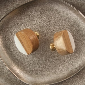 Op de afbeelding: Twee ronde houten knoppen met een witte halve cirkel op elk. De knoppen hebben een messing afwerking en worden gepresenteerd op een zilveren dienblad.