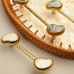 May include: A set of four gold cabinet knobs with a twisted metal stem. The knobs are made of iridescent mother of pearl with a gold rim.