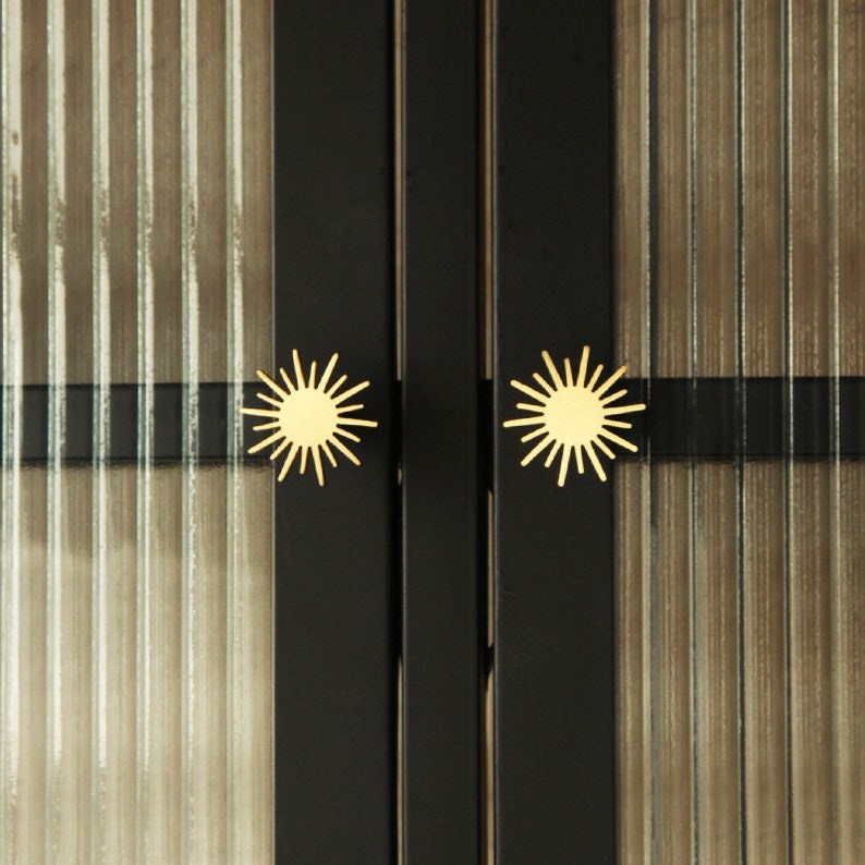 May include: Close-up of a black cabinet with two gold starburst-shaped door knobs.