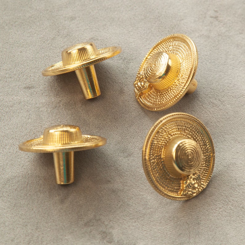 May include: Four gold-toned cabinet knobs shaped like miniature straw hats with a raised floral design.