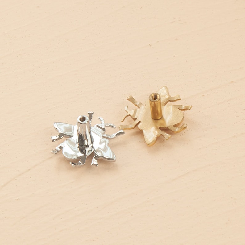 Peut inclure: Deux boutons de porte en forme d'abeille, l'un argent&eacute; et l'autre dor&eacute;. Les boutons sont vus du dessous, avec les trous de vis visibles.