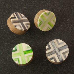 May include: Four round wooden knobs with geometric patterns. Two knobs have a green and white pattern, and two knobs have a black and white pattern.