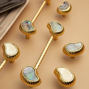 May include: Six gold cabinet knobs with a pearlescent shell inlay. The knobs have a decorative, fluted edge.