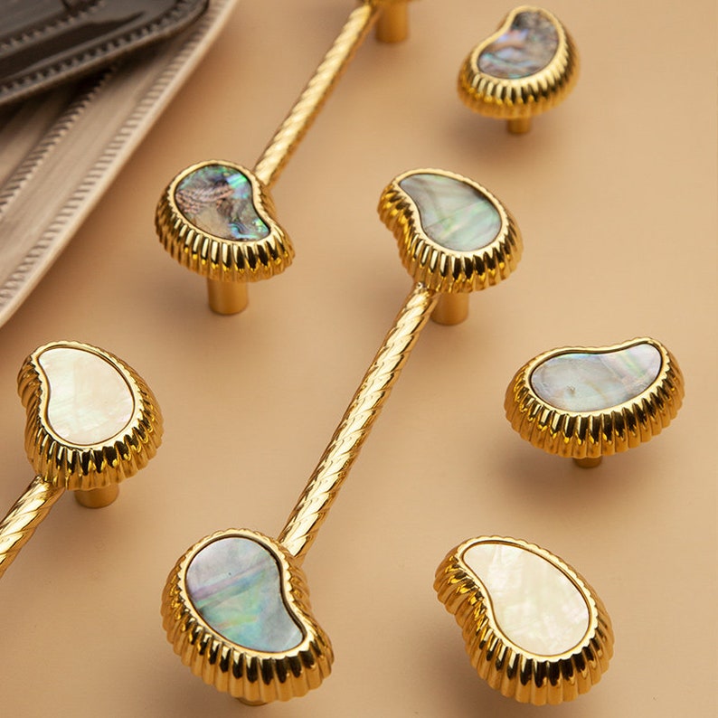 May include: Six gold cabinet knobs with a pearlescent shell inlay. The knobs have a decorative, fluted edge.