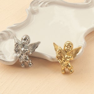 Könnte beinhalten: Zwei Cherub-Figuren, eine silber und eine gold, beide spielen ein Musikinstrument.