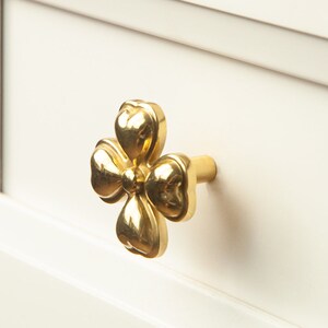 May include: A gold-toned flower-shaped drawer pull with a four-leaf clover design.