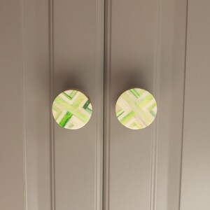 K&ouml;nnte beinhalten: Zwei runde, gr&uuml;ne und wei&szlig;e, gemusterte Schrankkn&ouml;pfe mit Holzsockel.