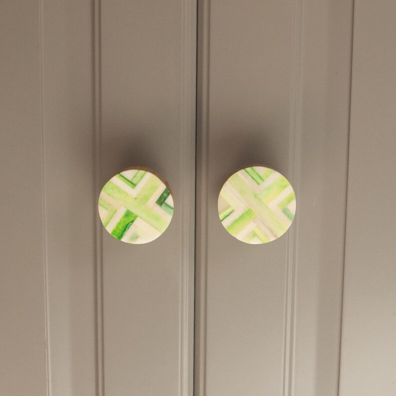 K&ouml;nnte beinhalten: Zwei runde, gr&uuml;ne und wei&szlig;e, gemusterte Schrankkn&ouml;pfe mit Holzsockel.