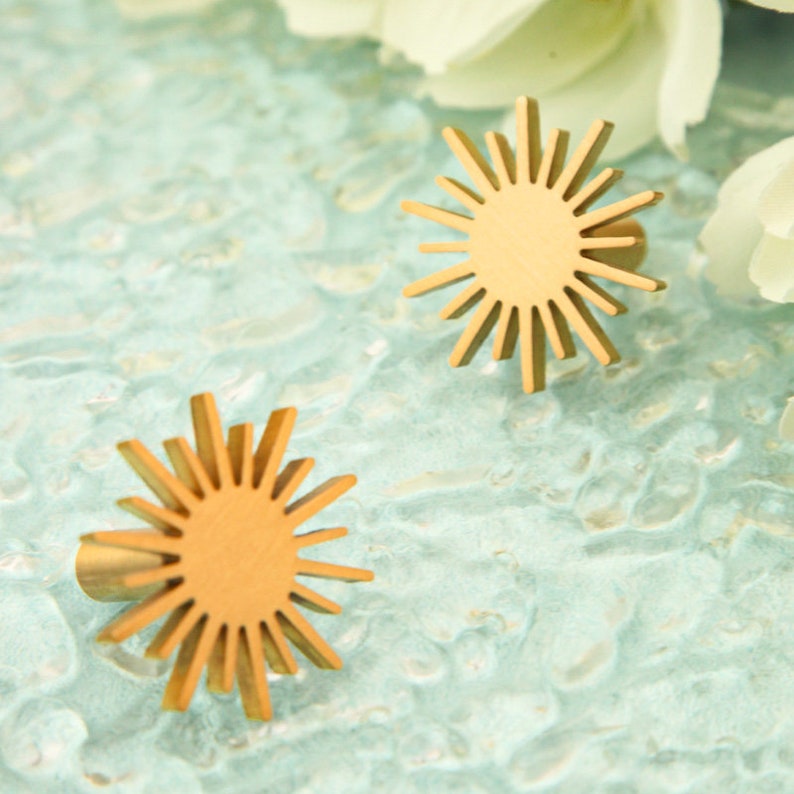 May include: Two gold-colored sunburst-shaped cabinet knobs with a circular center. The knobs are on a light blue textured surface.
