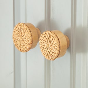 May include: Two round, woven rattan cabinet knobs with a natural wood base. The knobs are a light brown color and have a circular woven pattern.