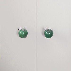 K&ouml;nnte beinhalten: Zwei gr&uuml;ne, apfelf&ouml;rmige Schrankkn&ouml;pfe mit silberfarbenen Blattakzenten. Die Kn&ouml;pfe sind auf einer hellgrauen Oberfl&auml;che montiert und bieten eine dekorative und funktionale Hardware-L&ouml;sung f&uuml;r M&ouml;bel.