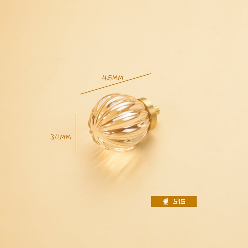 May include: A gold-toned cabinet knob with a clear glass sphere featuring a ribbed design. The knob measures 4.5 cm in diameter and 3.4 cm in height. The knob weighs 51 grams.