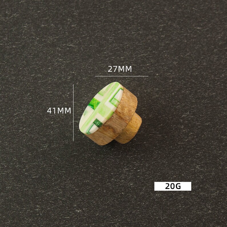 K&ouml;nnte beinhalten: Gr&uuml;ner und wei&szlig;er, gemusterter Holz-Knopf mit einem Durchmesser von 27 mm und einer H&ouml;he von 41 mm. Der Knopf wiegt 20 Gramm.