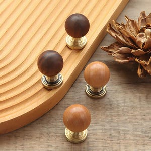 Peut inclure: Ensemble de quatre boutons ronds en bois avec des bases en laiton. Les boutons, de tons bruns variés, sont disposés sur une surface en bois sculpté. L'ensemble suggère un matériel décoratif ou fonctionnel, comme des poignées.