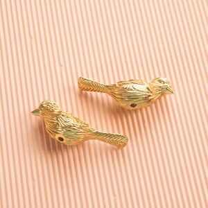 May include: Two gold-colored bird figurines with detailed textured surfaces. The birds are facing the same direction with their beaks open.