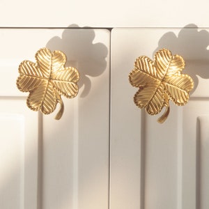 Peut inclure: Deux boutons de porte en forme de tr&egrave;fle &agrave; quatre feuilles de couleur or avec une finition textur&eacute;e.