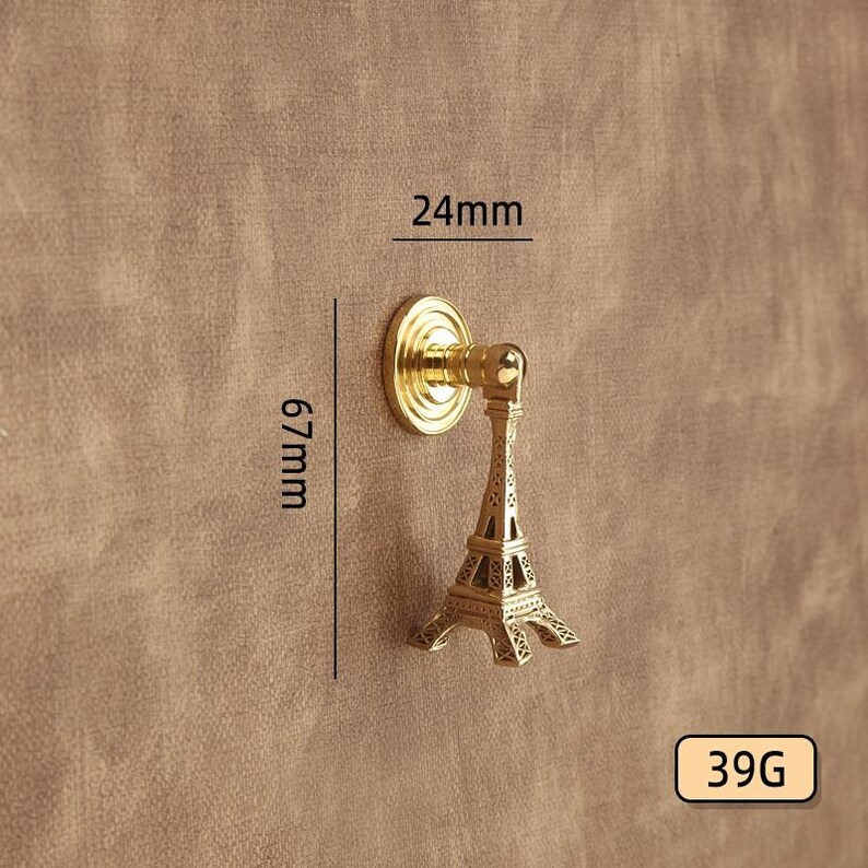 Peut inclure: Un bouton de meuble dor&eacute; avec un design de la Tour Eiffel. Le bouton mesure 24 mm de large et 67 mm de haut. Le poids est de 39g. Le bouton est mont&eacute; sur une surface marron.