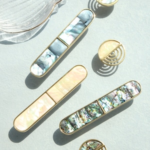 May include: Five decorative cabinet knobs with a gold finish and iridescent mother-of-pearl inlay. The knobs are in various shapes, including round, oval, and rectangular.