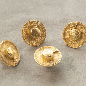 May include: Four gold-coloured metal hat-shaped buttons with a woven texture. The buttons have a raised design on the top.