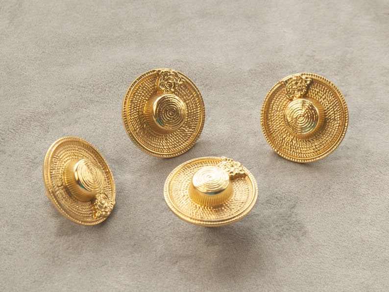 May include: Four gold-coloured metal hat-shaped buttons with a woven texture. The buttons have a raised design on the top.