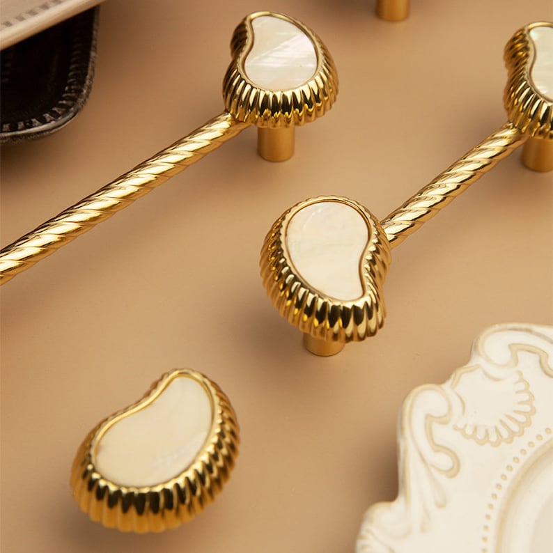 May include: Gold cabinet knobs with a pearlescent white shell inlay. The knobs have a rope-like design on the stem.