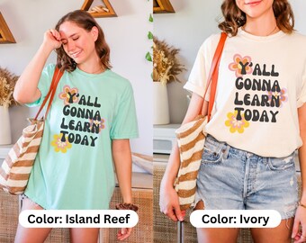 Op de afbeelding: Twee vrouwen dragen T-shirts met de tekst "Y'all Gonna Learn Today" in een retro-lettertype met bloemen. Het shirt aan de linkerkant is lichtblauw en het shirt aan de rechterkant is ivoor.