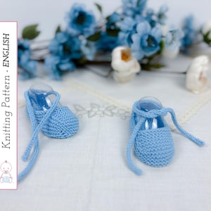 Puede incluir: Un par de patucos de bebé de punto azul claro con lazos largos, expuestos sobre una superficie blanca. El texto "Knitting Pattern - English" es visible a la izquierda de la imagen, junto con una pequeña ilustración.