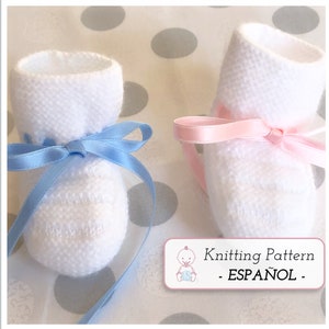 Puede incluir: Dos pares de botitas de bebé de punto blanco con lazos de cinta de satén. Un par tiene una cinta azul y el otro una cinta rosa. Las botitas están sobre un fondo blanco con lunares grises. Patrón de tejido - ESPAÑOL -
