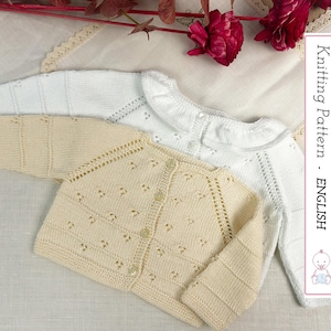 Puede incluir: Un patrón de tejido de punto en inglés para un cárdigan de bebé con un cuello de ganchillo blanco. El patrón se muestra sobre un fondo de tela blanca con flores rojas.