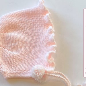Puede incluir: Un gorro de bebé de punto rosa con un pompón blanco y un borde rizado. El gorro tiene un cordón de ajuste y el texto "Knitting Pattern - ENGLISH" es visible en la imagen.