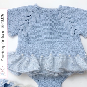May include: A pale blue knitted baby outfit featuring a ruffled skirt and decorative leaf patterns on the shoulders. The set includes a top, bottom, and matching booties. The text "Knitting Pattern - English" is visible on the left side.