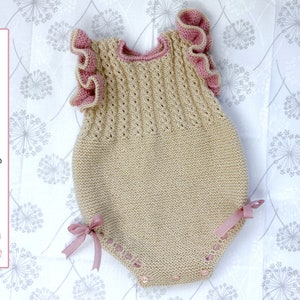 Könnte beinhalten: Ein gestrickter Baby-Strampler mit beigefarbenem Oberteil und rosa Rüschenärmeln. Der Strampler hat ein zartes Spitzenmuster und ist mit rosa Bändern an den Schultern gebunden.