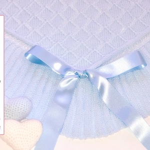 May include: A light blue knitted baby blanket with a satin ribbon tied in a bow. The blanket has a diamond pattern and a ruffled edge.