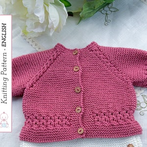 May include: A pink knitted baby cardigan with short sleeves and button closures. The cardigan has a delicate lace trim around the neckline and bottom hem. Knitting Pattern - ENGLISH.