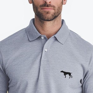Puede incluir: Una camiseta polo gris con una silueta negra de un perro en el pecho izquierdo.