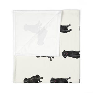May include: A white throw blanket with a repeating pattern of black Labrador Retriever dogs in various poses. The blanket has a soft, plush texture.