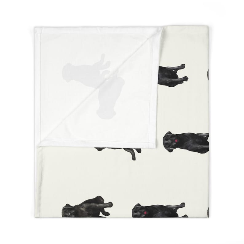 May include: A white throw blanket with a repeating pattern of black Labrador Retriever dogs in various poses. The blanket has a soft, plush texture.