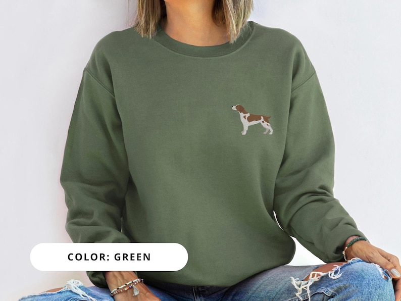 May include: A green sweatshirt with a brown and white dog illustration on the front. The text "COLOR: GREEN" is printed below the image.
