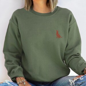 May include: A green sweatshirt with a small, red silhouette of a dog sitting on the left chest.