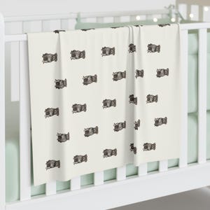 Pu&ograve; includere: Una coperta per bambini color crema con un motivo ripetuto di illustrazioni di animali grigio scuro. La coperta &egrave; drappeggiata su una culla bianca, con un colore di accento verde chiaro visibile sullo sfondo.
