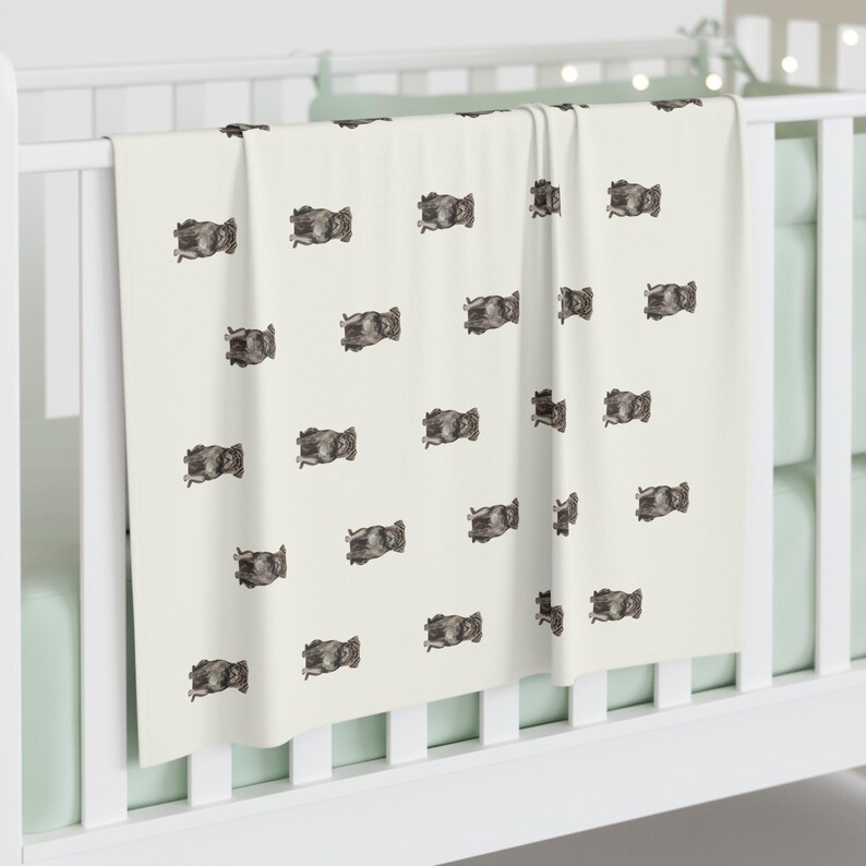 Pu&ograve; includere: Una coperta per bambini color crema con un motivo ripetuto di illustrazioni di animali grigio scuro. La coperta &egrave; drappeggiata su una culla bianca, con un colore di accento verde chiaro visibile sullo sfondo.