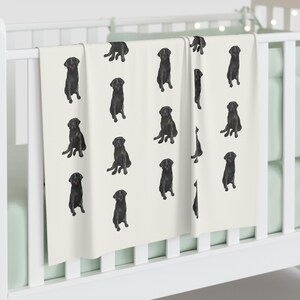 May include: A white baby blanket with a black Labrador Retriever pattern. The blanket features a repeating pattern of black Labrador Retrievers sitting on a white background.