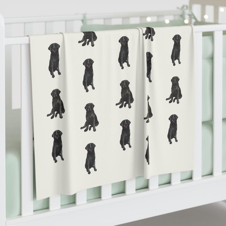 May include: A white baby blanket with a black Labrador Retriever pattern. The blanket features a repeating pattern of black Labrador Retrievers sitting on a white background.