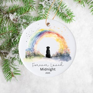 May include: A white ceramic ornament featuring a watercolor rainbow and a black silhouette of a dog. The text "Forever Loved", "Midnight", and the year 2025 are written below the dog. A gold string is attached for hanging.