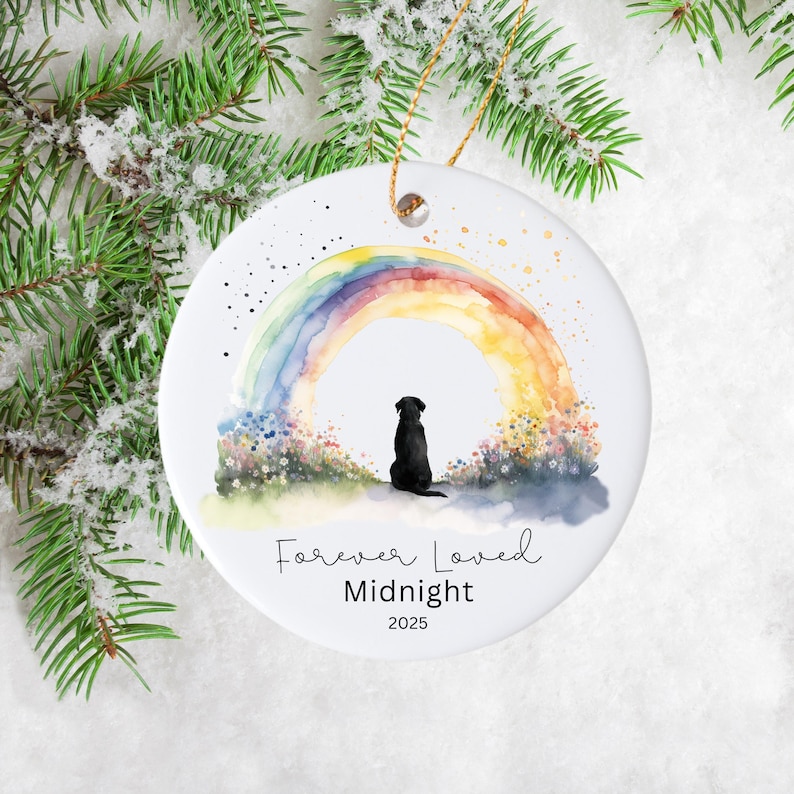 May include: A white ceramic ornament featuring a watercolor rainbow and a black silhouette of a dog. The text "Forever Loved", "Midnight", and the year 2025 are written below the dog. A gold string is attached for hanging.