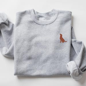 May include: A gray sweatshirt with a brown dog silhouette embroidered on the front. The dog is looking up and has a red collar.