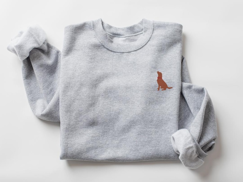 May include: A gray sweatshirt with a brown dog silhouette embroidered on the front. The dog is looking up and has a red collar.